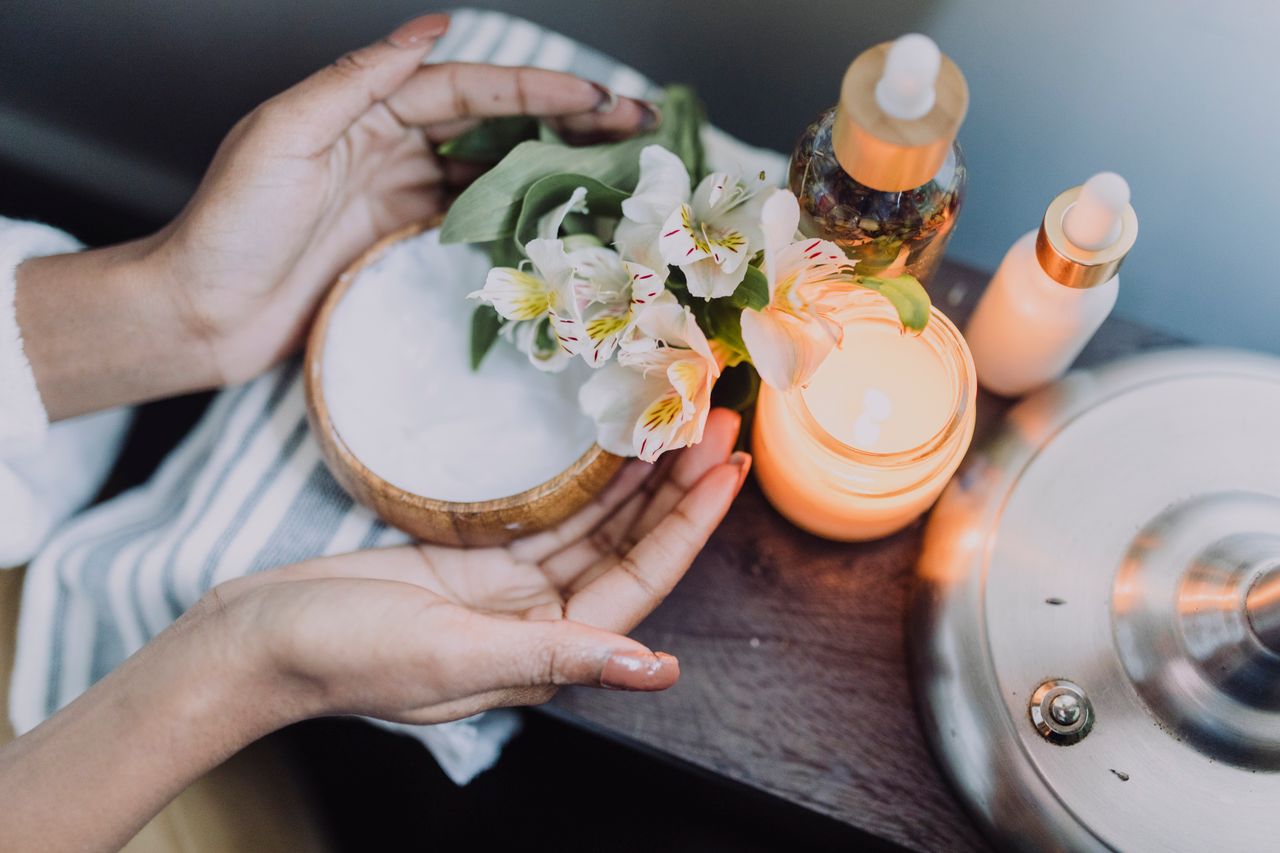 Services A calming spa scene featuring hands holding flowers beside candles and skincare products.