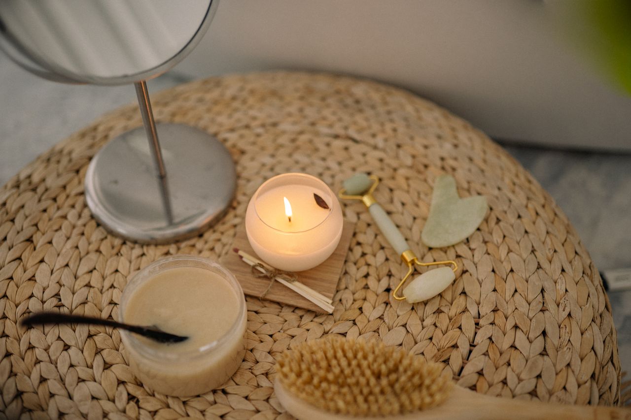 Services A serene spa setup featuring a lit candle, jade face roller, and body scrub on a woven mat.